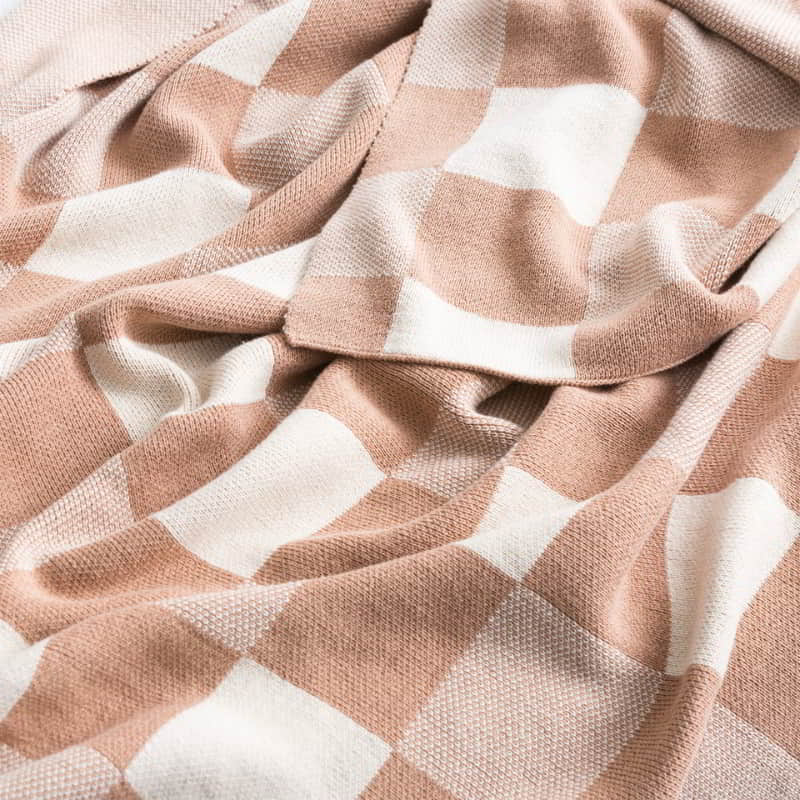 alt="Zoom in details of a shade of tan with yarn-dyed cotton knitted blanket with large checks design in French blue. Ultra-soft and cosy texture, perfect for any decor style."