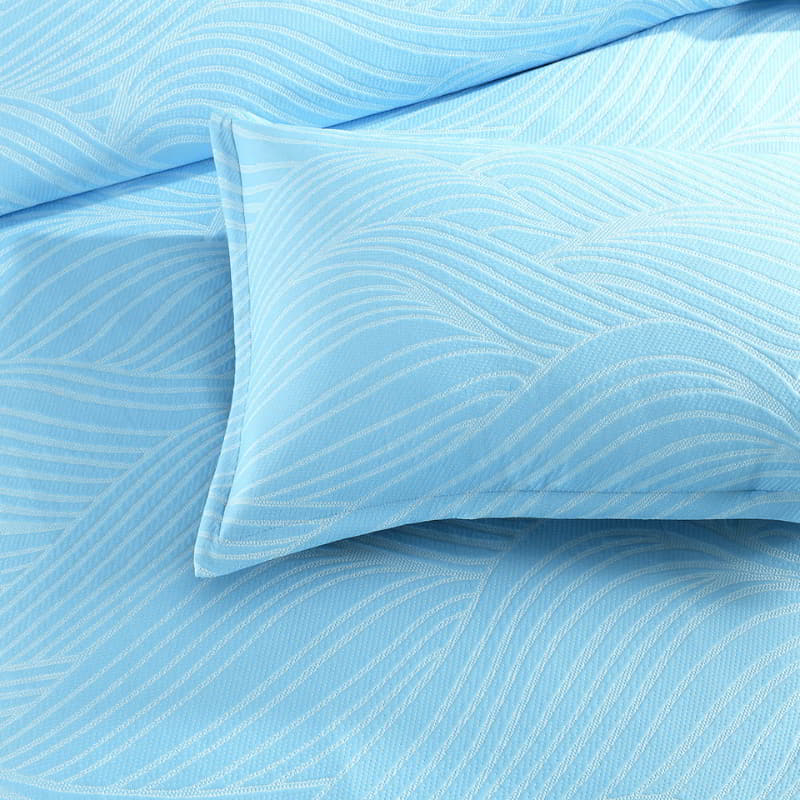 alt="Close-up details of a shades of blue quilt cover with a beach wave design."