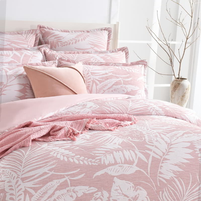 alt="Showcasing a shade of pink european pillowcase and quilt cover featuring intricate island themes with swaying palm trees in tropical rainforest in a cosy bedroom"