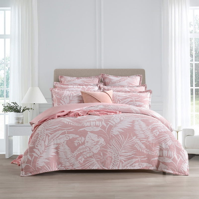 alt="Showcasing a shade of pink European pillowcase featuring intricate island themes with swaying palm trees in a tropical rainforest, paired with the beautiful quilt cover in a cosy bedroom."