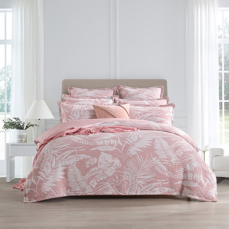 alt="Showcasing a shade of pink quilt cover featuring intricate island themes with swaying palm trees in tropical rainforest in a cosy bedroom"