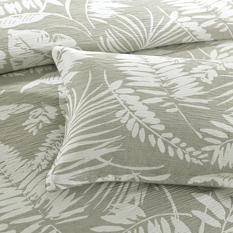 alt="A shade of sage green quilt cover featuring intricate island themes with swaying palm trees in a tropical rainforest with the pillowcases."