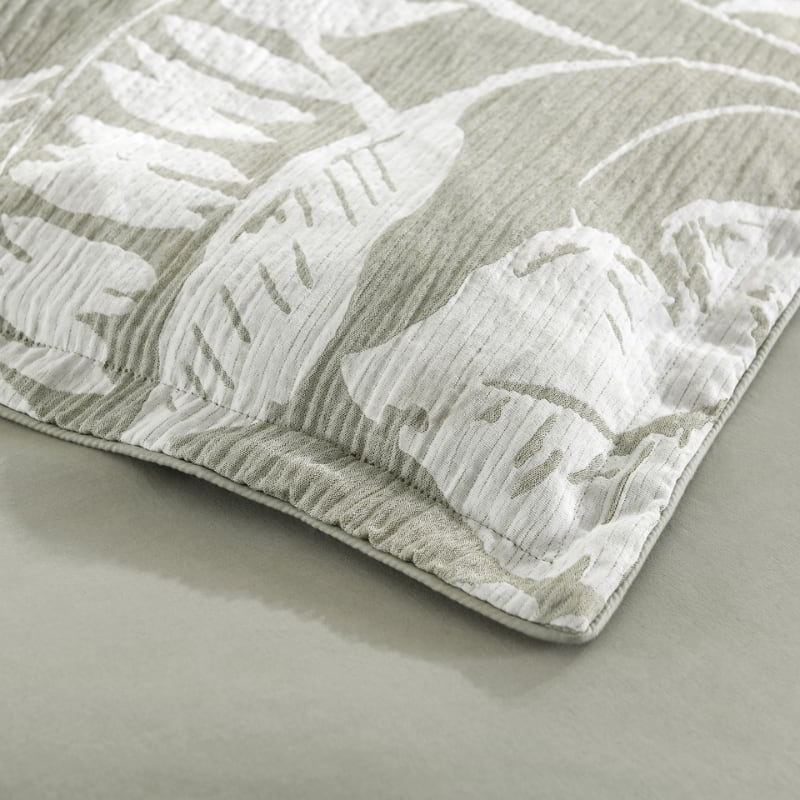 alt="Zoom in details of a shade of sage green pillowcase featuring intricate island themes with swaying palm trees in a tropical rainforest in a cosy bedroom"
