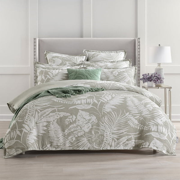 alt="Showcasing a shade of sage green quilt cover featuring intricate island themes with swaying palm trees in a tropical rainforest."