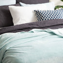 An indulgent bed, generously proportioned, adorned with a pristine  blue velvet blanket and plush pillows