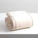 A sumptuous, generously-sized, ultra-soft sand colour velvet blanket, elegantly folded on a pristine white surface.