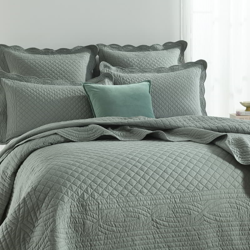 alt="Green coverlet and pillowcases set with a nod to French quilting tradition and decorative details like scallop edges in a cosy bedroom"