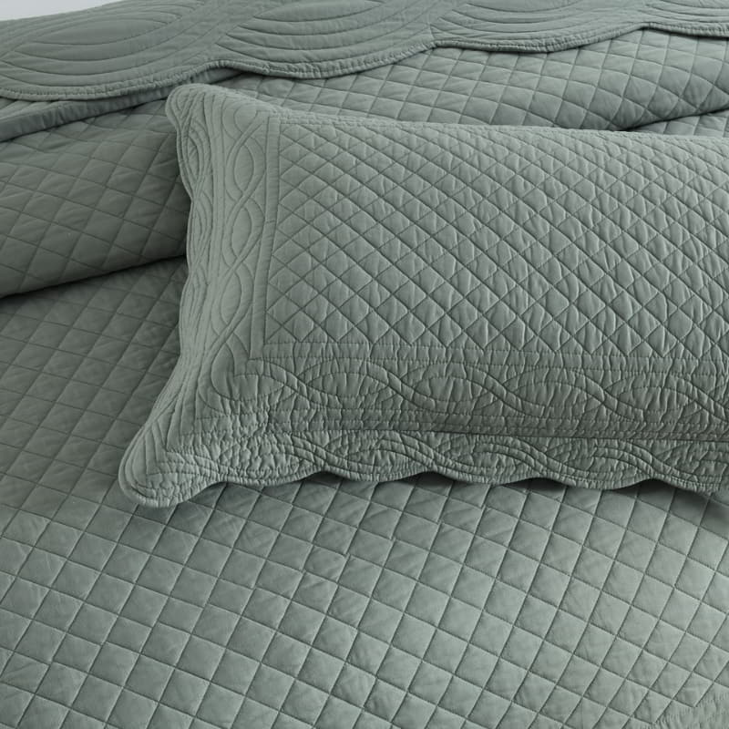 alt="Showcasing a green coverlet and pillowcases set with a nod to French quilting tradition and decorative details like scallop edges in a cosy bedroom"