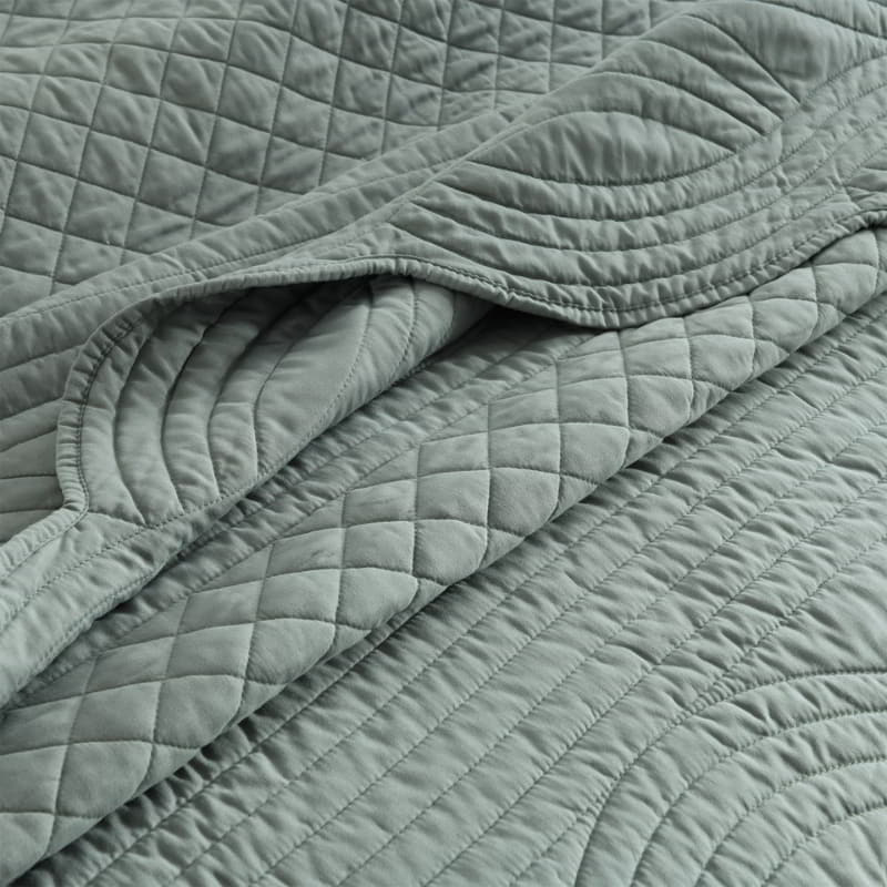 alt="Close up details of a green coverlet set with a nod to French quilting tradition and decorative details like scallop edges"