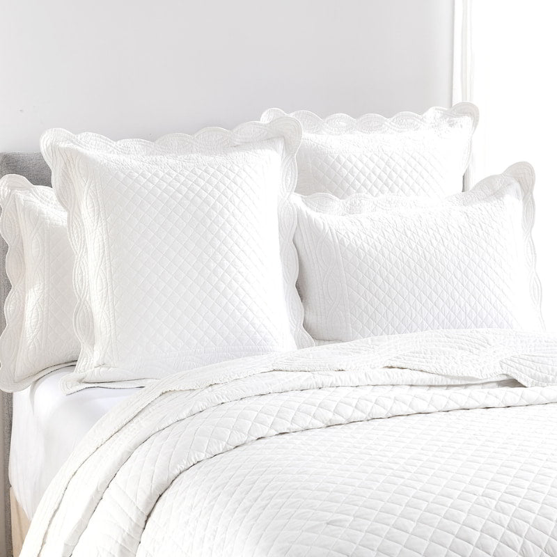 alt="Shade of white coverlet set with a nod to French quilting tradition and decorative details like scallop edges in a luxurious bedroom"