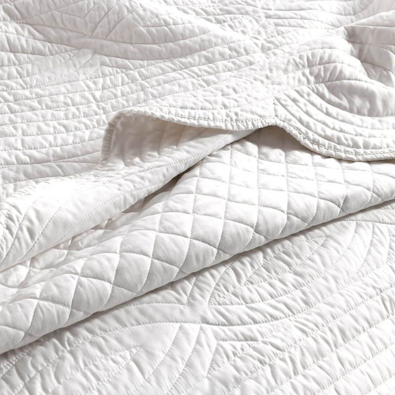 alt="Closer look of a white coverlet set with a nod to French quilting tradition and decorative details like scallop edges"