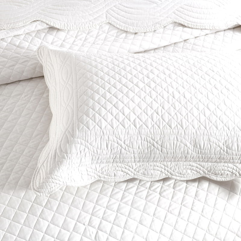 alt="Zoom in details of a white coverlet set and pillowcase with a nod to French quilting tradition and decorative details like scallop edges"