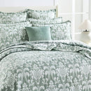 alt="Showcasing elegant coverlet pairing with the pillows boasting a timeless jade and white damask pattern, highlighted by sharp, straight piped edge detailing in a luxurious bedroom."