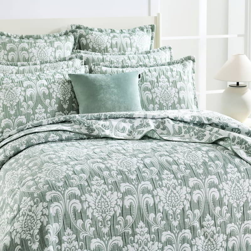 alt="Showcasing elegant coverlet pairing with the pillows boasting a timeless jade and white damask pattern, highlighted by sharp, straight piped edge detailing in a luxurious bedroom."