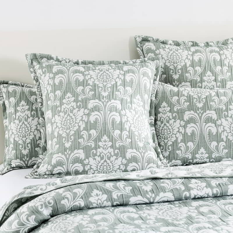 alt="Elegant coverlet and pillows boasting a timeless jade and white damask pattern, highlighted by sharp, straight piped edge detailing in a luxurious bedroom."