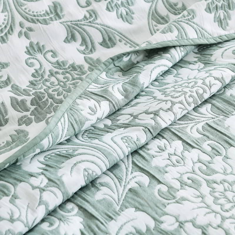 alt="Zoom in details of elegant coverlet boasting a timeless jade and white damask pattern, highlighted by sharp, straight piped edge detailing."