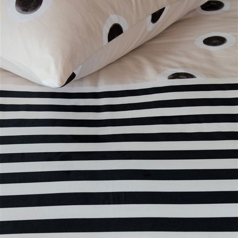 alt="Close-up look of a dotted and striped quilt cover with hand-painted black and white dots on a cream background on the top side and horizontal black and white stripes on the underside"