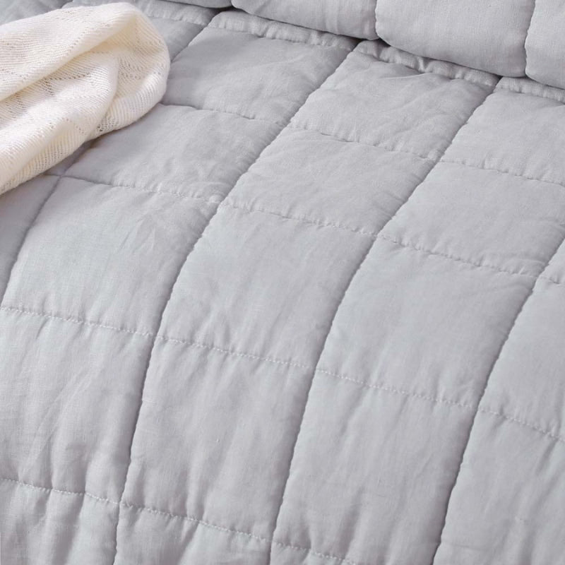 alt="A close up look of a french linen coverlet set with 2 quilted pillowcases."