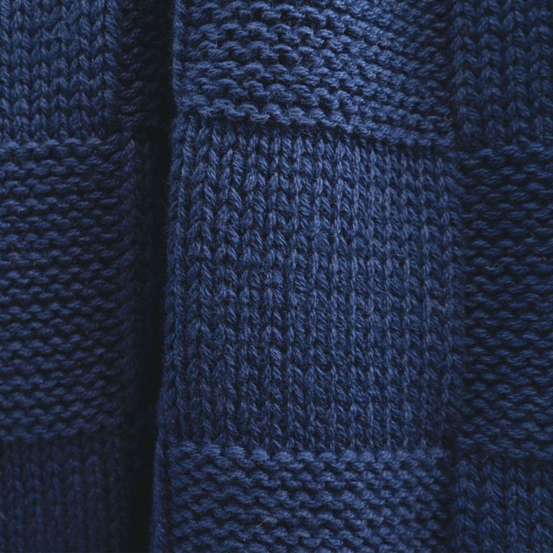 Close-up of the knitted texture and square pattern on the navy throw.