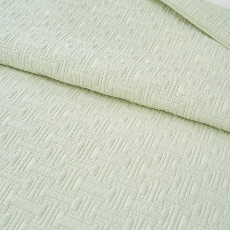 Lightweight cotton coverlet in soothing green draped neatly over a bed.