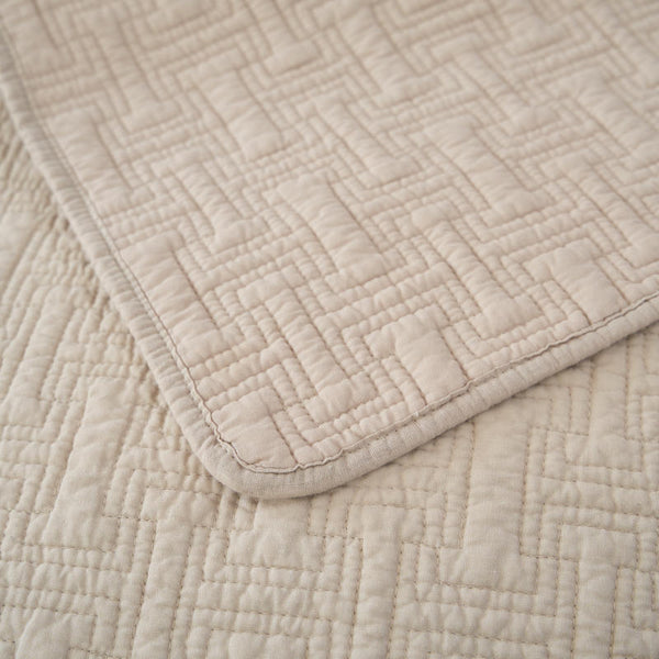 Soft neutral cotton throw with detailed stitching and bound edges.