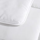 Rolled white microfibre quilt on plain background.