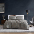 Kenneth Cole Sussex Khaki/Black Quilt Cover Set styled on bed with dark navy wall and wooden bedside table.