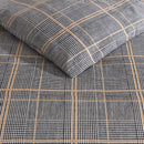 Kenneth Cole Sussex Khaki/Black Quilt Cover Set styled on bed with dark navy wall and wooden bedside table.