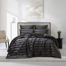 A modern bedroom features the Morgan and Reid Black Velvet Stripe Snuggle Fleece Comforter Set on a neatly made bed with striped pillows, neutral walls, abstract art, a beige chair, round black side table with white flowers, and a lamp.