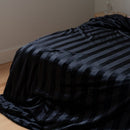 Black striped blanket on a bed in a room with neutral walls.