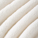 A neatly made bed showcases the Morgan and Reid Checkered Cream Snuggle Fleece Comforter Set with textured pillows, against a light wall, paired with a wooden headboard, bedside table, lamp, and a large leafy plant.