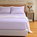 Bed with lavender bedding and pillows in a bedroom setting.