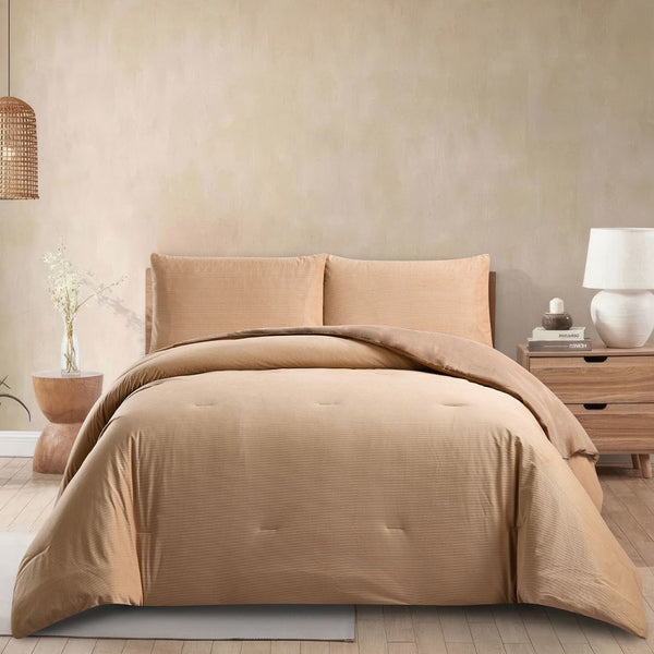 Beige bedding set on a bed in a bedroom with a lamp and plant in the background.