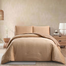 Beige bedding set on a bed in a bedroom with a lamp and plant in the background.
