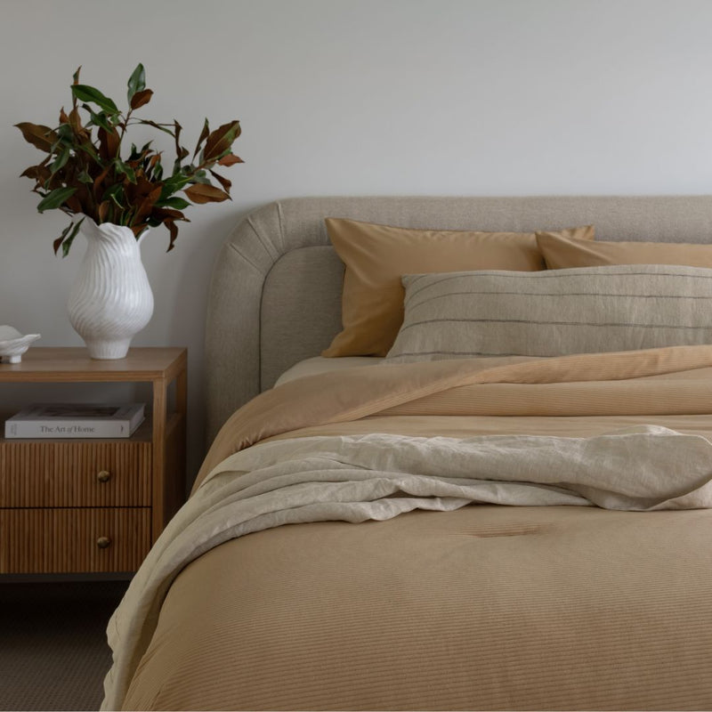 Neatly made bed with beige bedding in a bedroom setting.