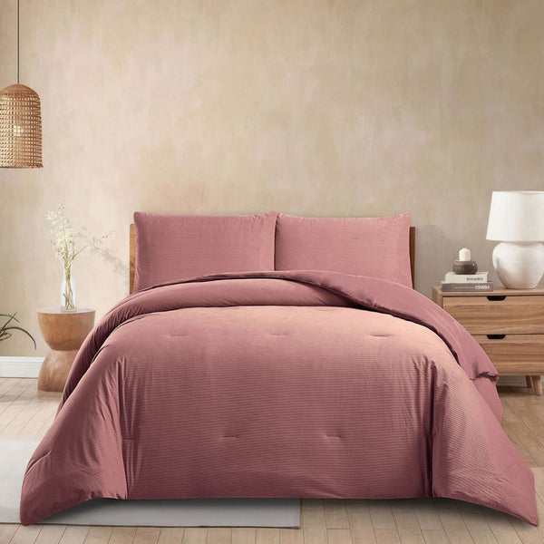Pink bedding set on a bed in a bedroom with a lamp and plant in the background.
