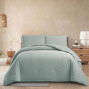 Teal comforter set on a bed in a bedroom setting with a lamp and plant.