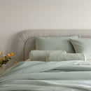 Bed with light blue bedding and pillows against a neutral wall.