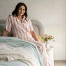 Woman in a striped nightshirt sitting on a bed with a vase of flowers in the background