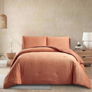 Orange bedding set on a bed in a room with a lamp and plant.