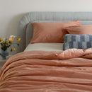Bed with pink orange bedding and pillows, featuring a vase of flowers on the nightstand.