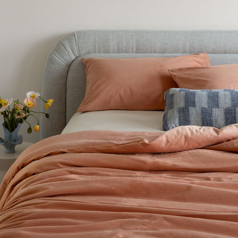 Bed with pink orange bedding and pillows, featuring a vase of flowers on the nightstand.