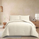 Beige comforter set on a bed in a bedroom setting with a lamp and plant.