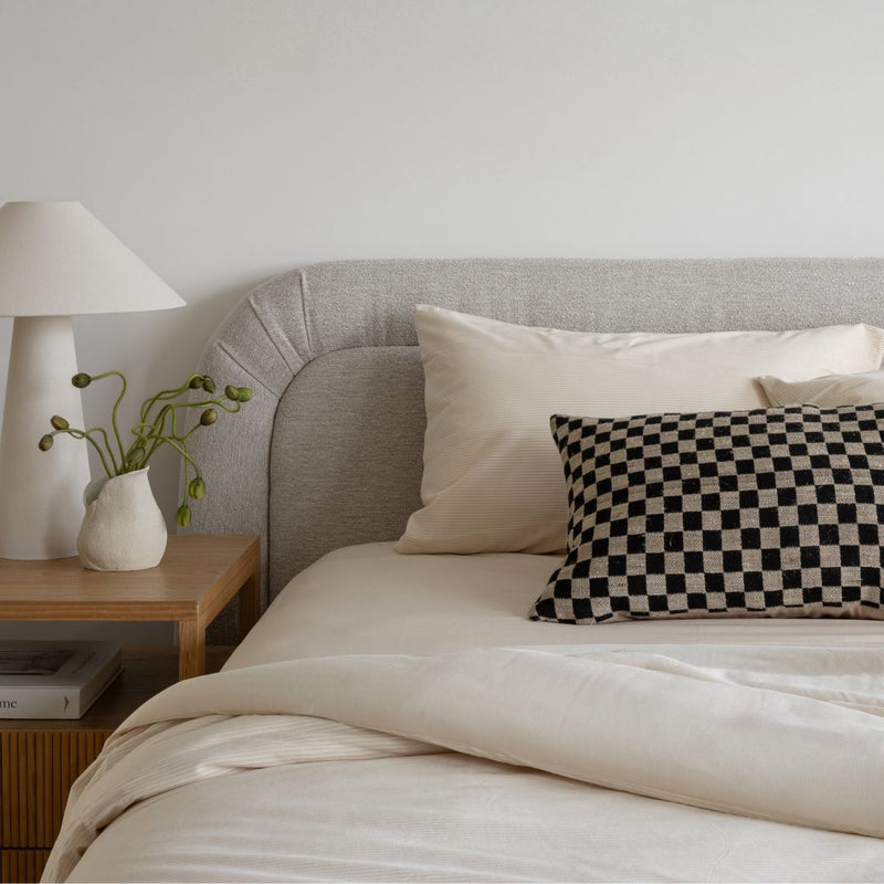 Neatly made bed with checkered pillow and lamp on nightstand in a bedroom setting