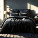 A black velvet comforter set on a bed, with a single pillowcase displayed. The comforter appears plush and is laid out in a room with a window allowing natural light to come in.