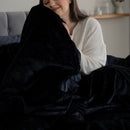 Person wrapped in a dark blanket on a couch in a cozy living room.