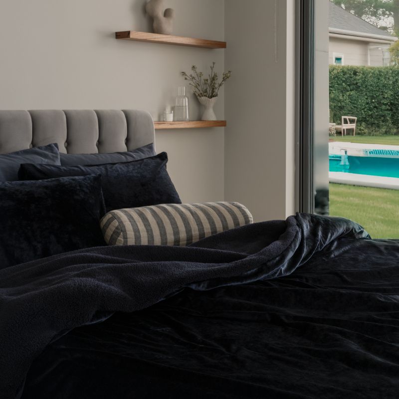 Bedroom with dark bedding and striped pillow, view of pool area through window.