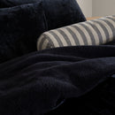 Black blanket draped over a striped cylindrical pillow on a dark surface.
