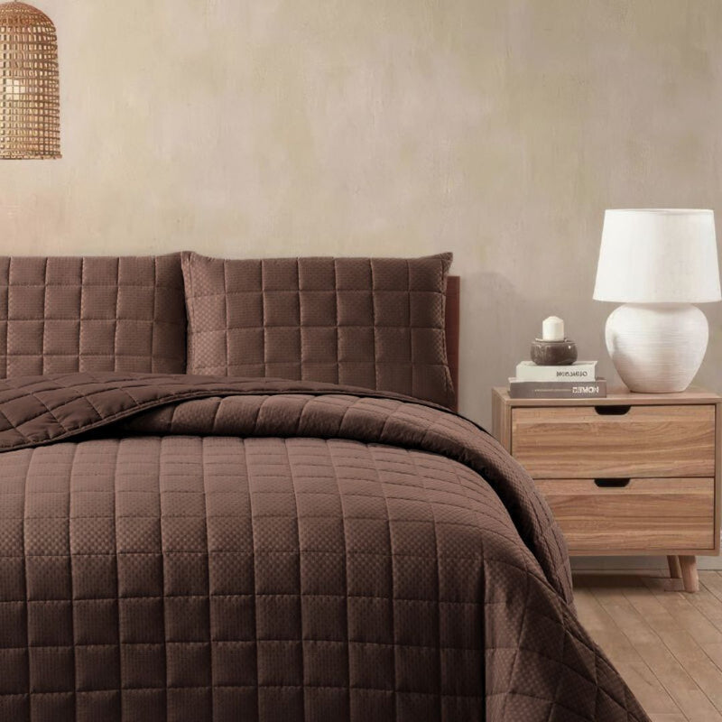 Brown quilted bedding set on a bed with a wooden nightstand and lamp in a bedroom setting.
