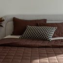 Brown quilt and pillows on a sofa against a neutral wall